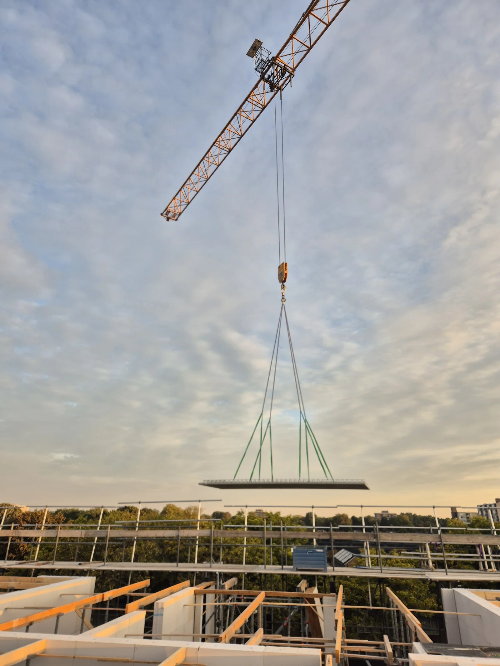 Constructief betonwerk bij zonsondergang: kraan hijst een prefab element op het dak